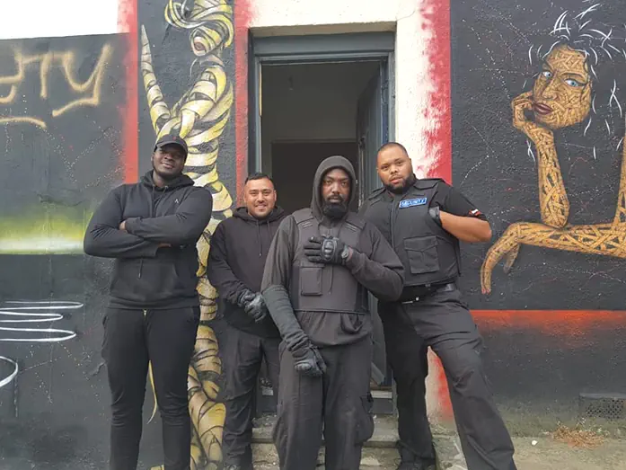 Bailiffs standing outside a public house with graffiti on the wall