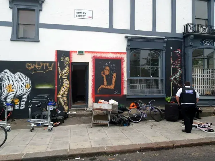 A bailiff standing outside a public house with graffiti on the wall and rubbish on thepavement